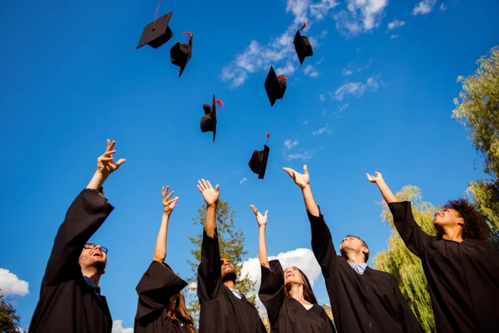 Graduates in gowns throw their graduation caps into the air on a clear day.